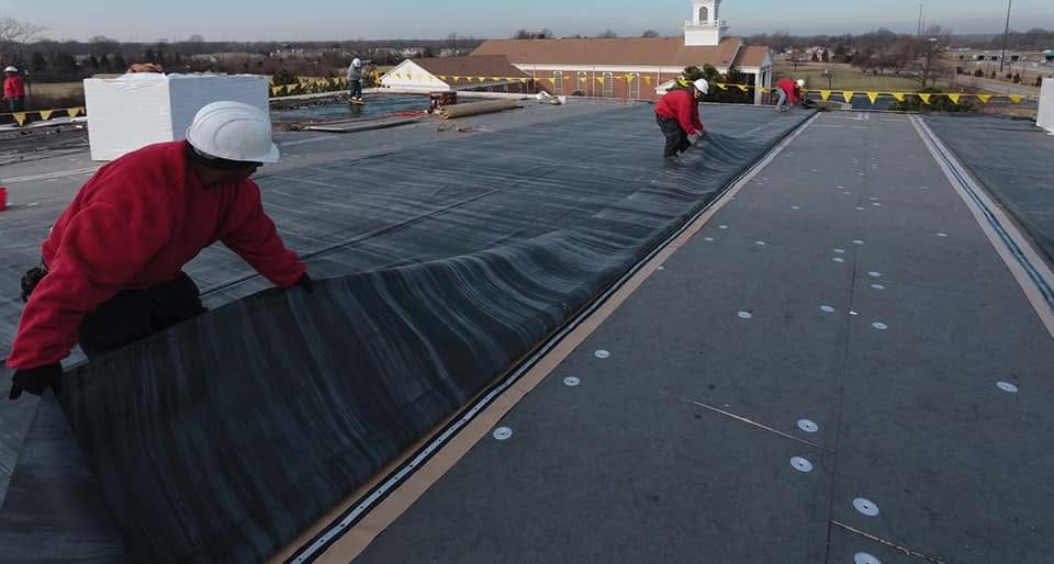Crew in hard hats laying membrane on a large commercial roof