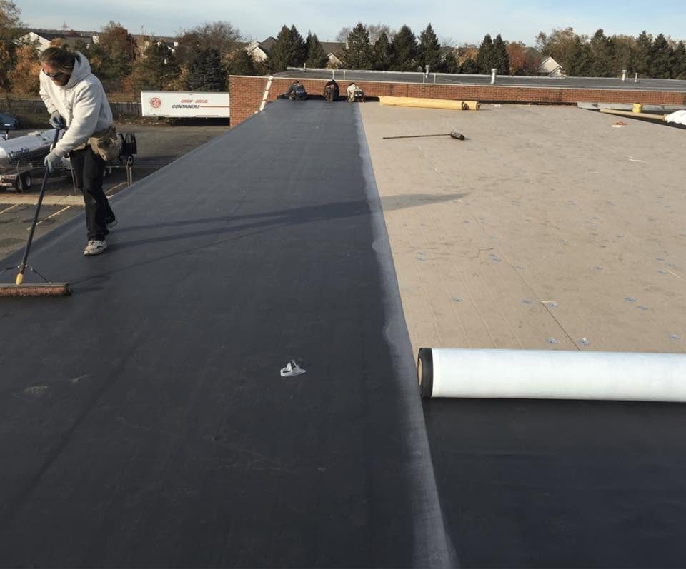 Roofer rolling out a new membrane over insulation board
