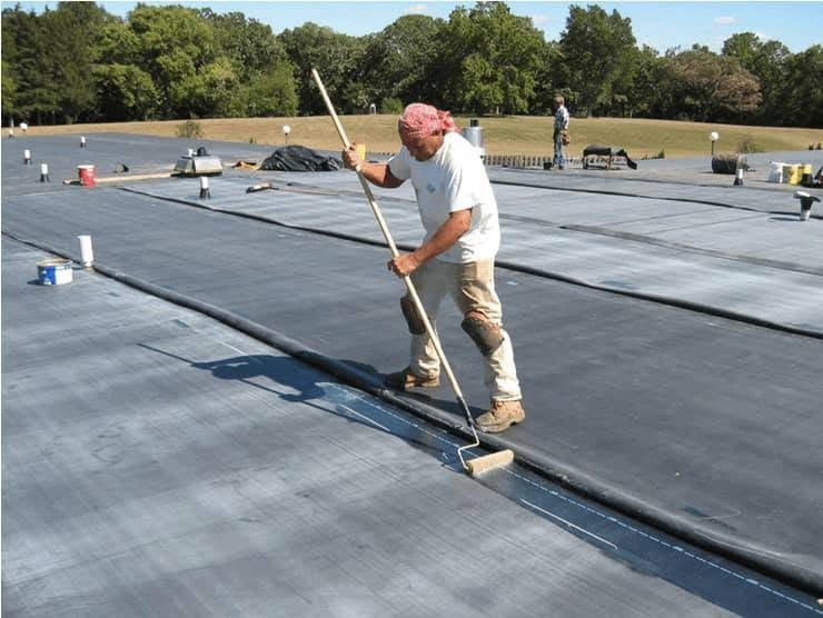 Roofer priming a membrane seam with a long brush