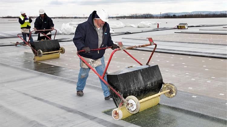 Crew rolling seams on a membrane roof with weighted rollers